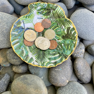 Monstera leaf shell dish holding assorted coins on river rocks